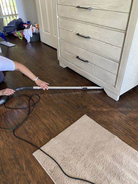 a house cleaning service vacuuming dust under a dresser