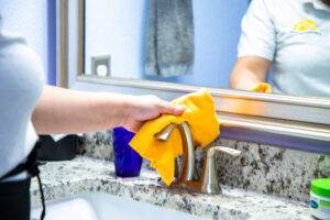 Photo of Dallas Sunrise Maids focusing on Home cleaning while polishing a chrome fixture in a bathroom using a microfiber cloth.