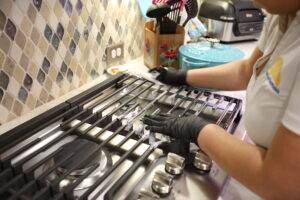 Image showing one of our house cleaners wearing gloves, doing a home cleaning focusing on the oven grate