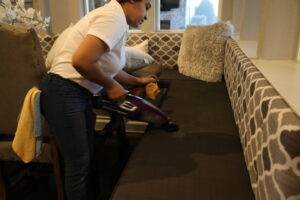 House cleaner holding a vacuum, cleaning the sofa in Plano, TX | Dallas Sunrise Maids