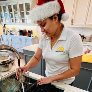 Dallas Sunrise Maids team member wearing a santa hat, using a sink to wash dishes for house cleaning in Plano, TX