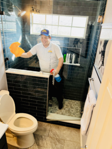 Image of a house cleaner in his Dallas Sunrise Maids uniform cleaning a shower.