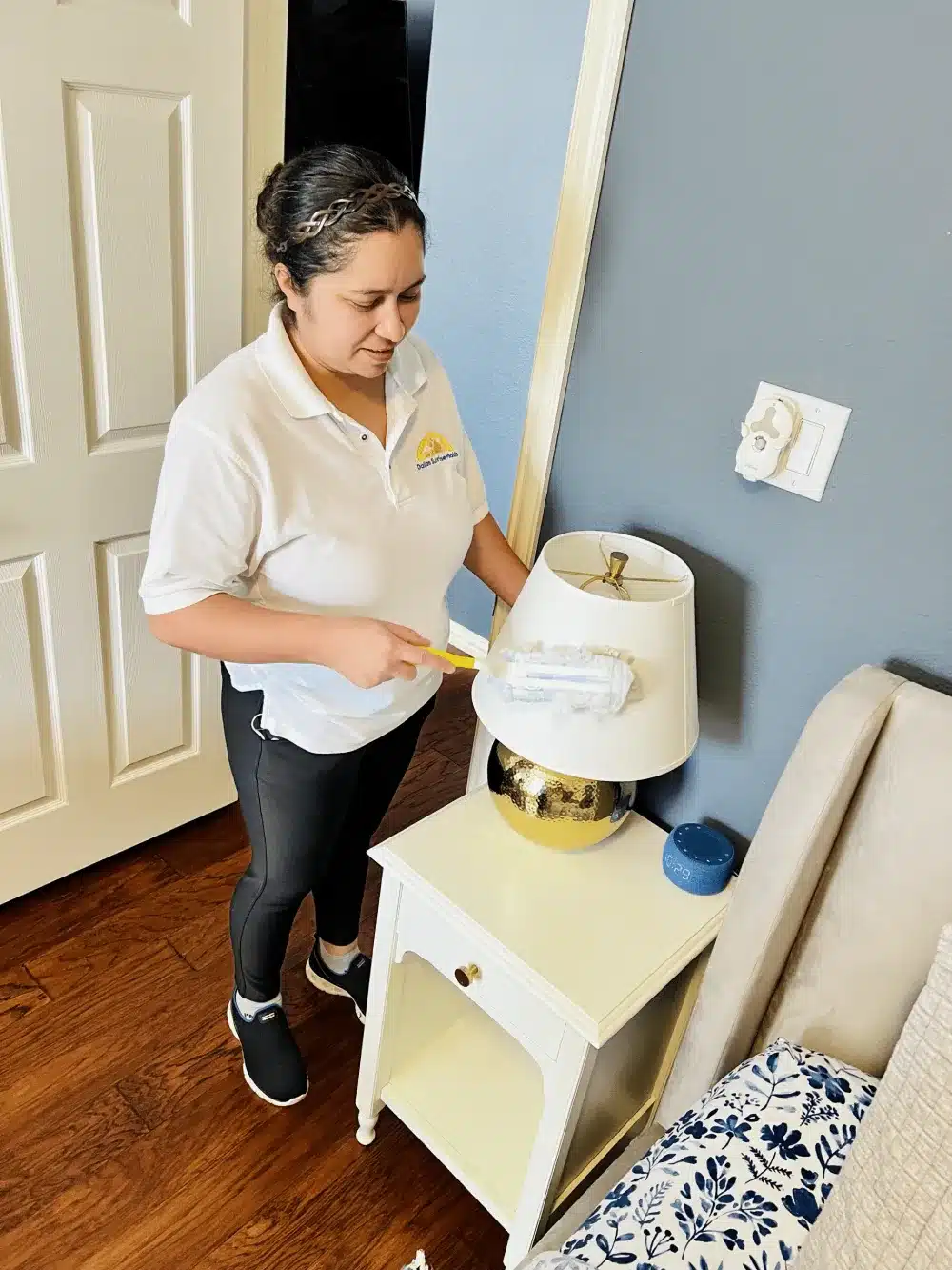 Professional house cleaner dusting a bedside lamp as part of quality cleaning service—illustrating how to give feedback to your house cleaner by Dallas Sunrise Maids in Plano, TX