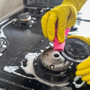Hands in gloves deep cleaning a greasy stove during a move-in cleaning in Dallas kitchen