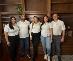 The Dallas Sunrise Maids team stands together in front of a wooden bookshelf wearing branded white shirts in Plano, TX