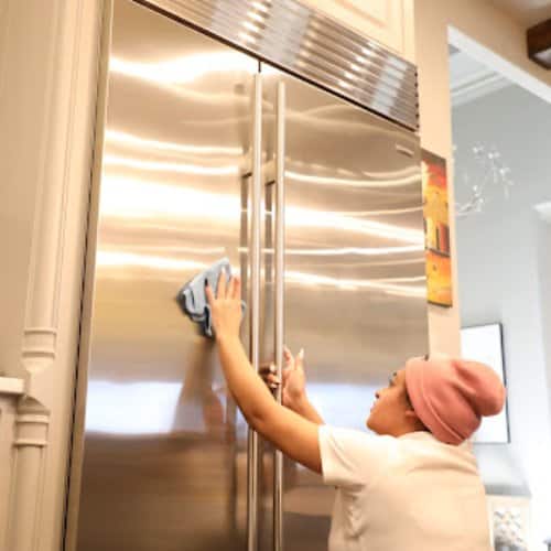 House cleaner wiping stainless steel refrigerator during deep cleaning by Dallas Sunrise Maids in Allen