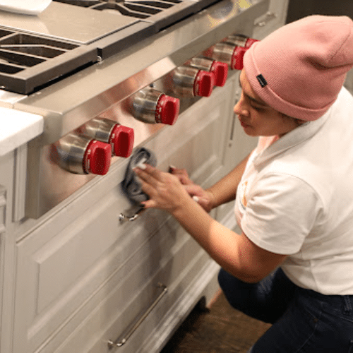 Professional house cleaning service in McKinney by Dallas Sunrise Maids, showing a cleaner polishing a stainless steel kitchen stove for a spotless finish
