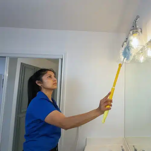 House cleaner dusting light fixture professionally by Dallas Sunrise Maids in Texas