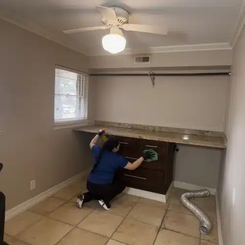 Professional house cleaner wiping and disinfecting cabinet drawers in a laundry or utility room during a home cleaning service by Dallas Sunrise Maids in Plano, TX.