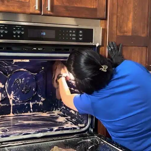 Gloved house cleaner scrubs a soapy oven interior for deep cleaning Plano TX by Dallas Sunrise Maids in Plano TX