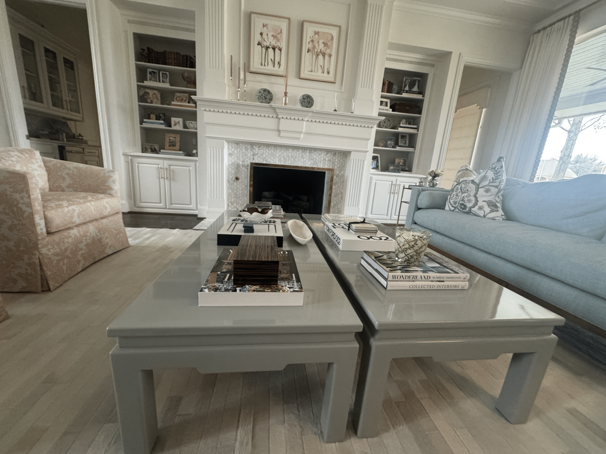 Two glossy gray coffee tables stacked with decorative books in a clean living room featuring built-in shelves and a white mantel, illustrating home cleaning in Plano, Texas by Dallas Sunrise Maids.