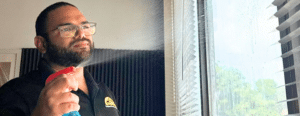 Jason Flores sunrise maids team member spraying a cleaning solution onto window glass with blinds raised, demonstrating home cleaning in Plano, Texas by Dallas Sunrise Maids.